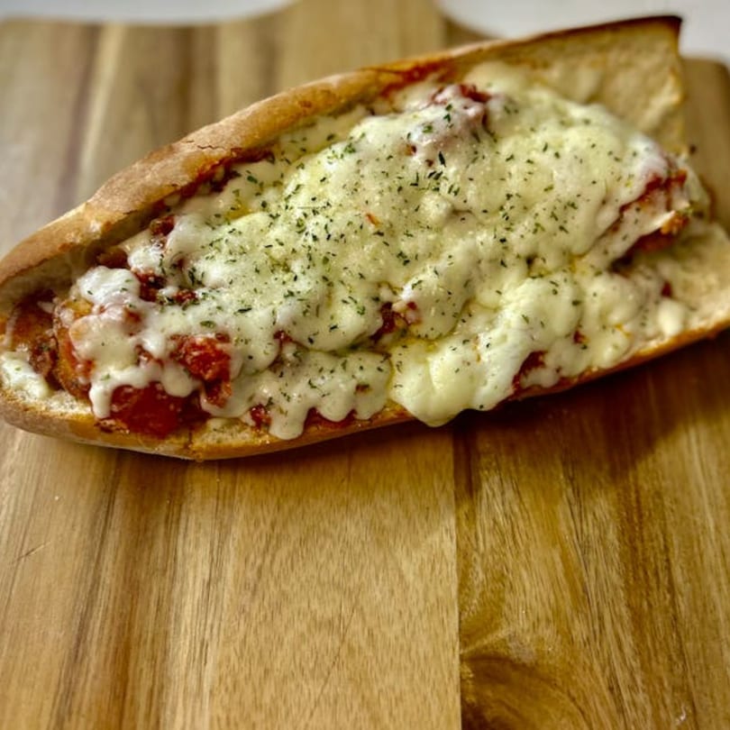 A South Shore Pizza meatball sub, generously topped with melted mozzarella cheese and herbs, on a wooden board.