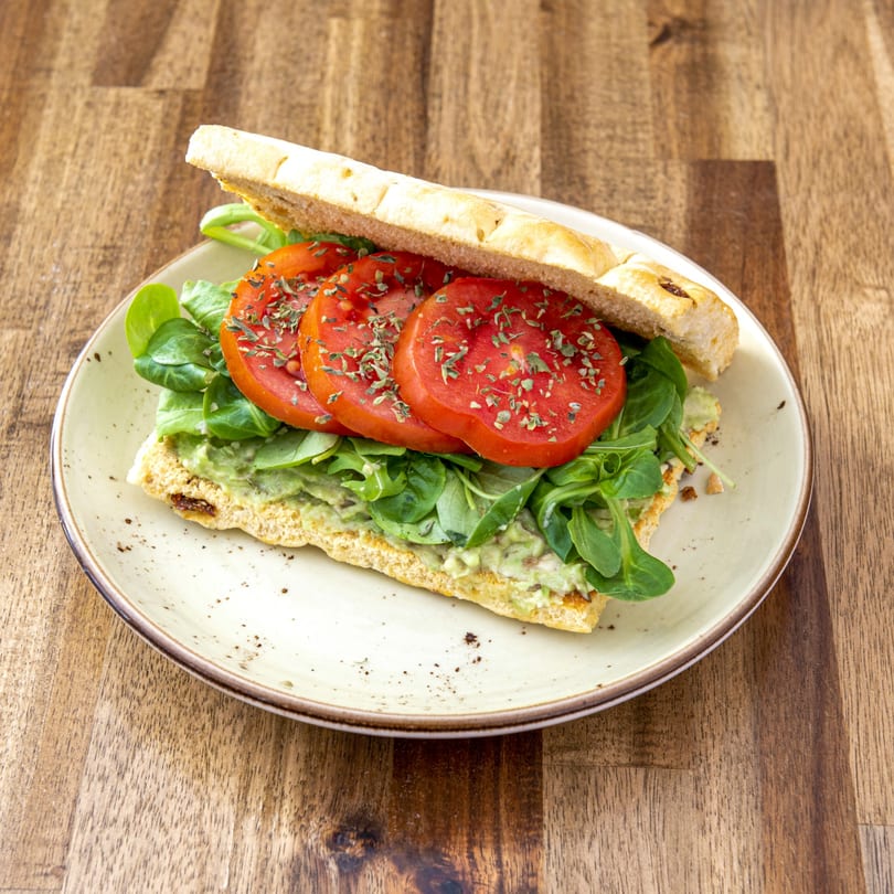 Open-faced sandwich with sliced tomatoes, green lettuce, and guacamole on a rustic plate.