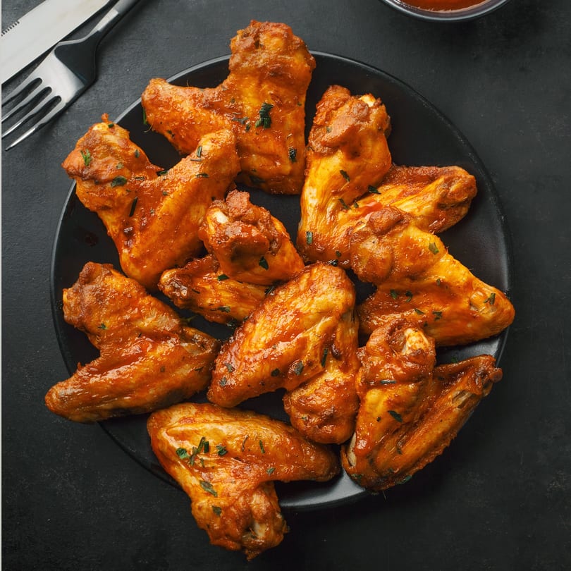A black plate filled with South Shore Pizza's buffalo chicken wings, garnished with herbs, next to cutlery.