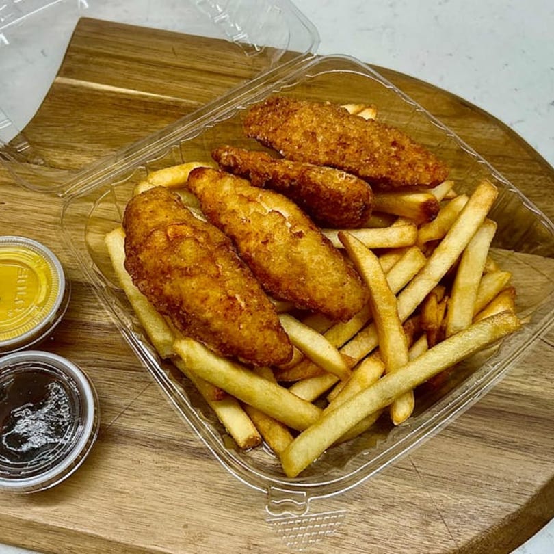 Crispy chicken tenders and golden french fries in a clear takeout container with dipping sauces.