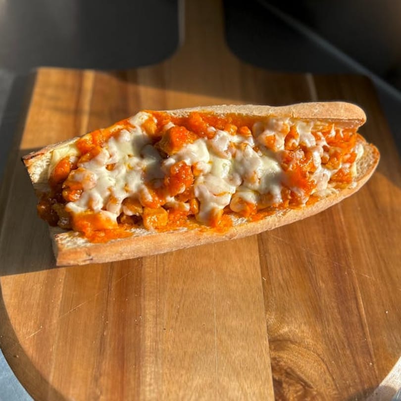 A buffalo chicken sub sandwich, topped with melted mozzarella cheese and orange sauce, on a wooden board.