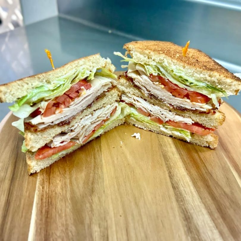 Two halves of a turkey club sandwich with lettuce, tomato, and bacon on toasted bread.