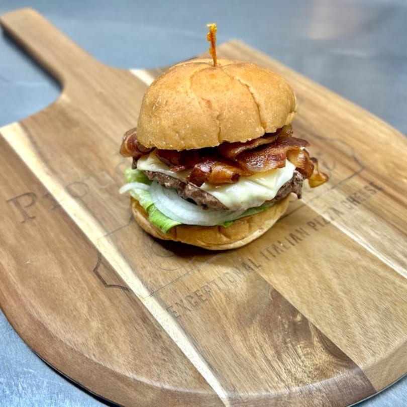 Bacon cheeseburger with lettuce and onion on a wooden pizza peel.